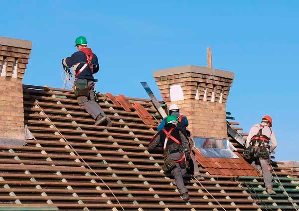 Three workers on a wood roof installing light brown tiles